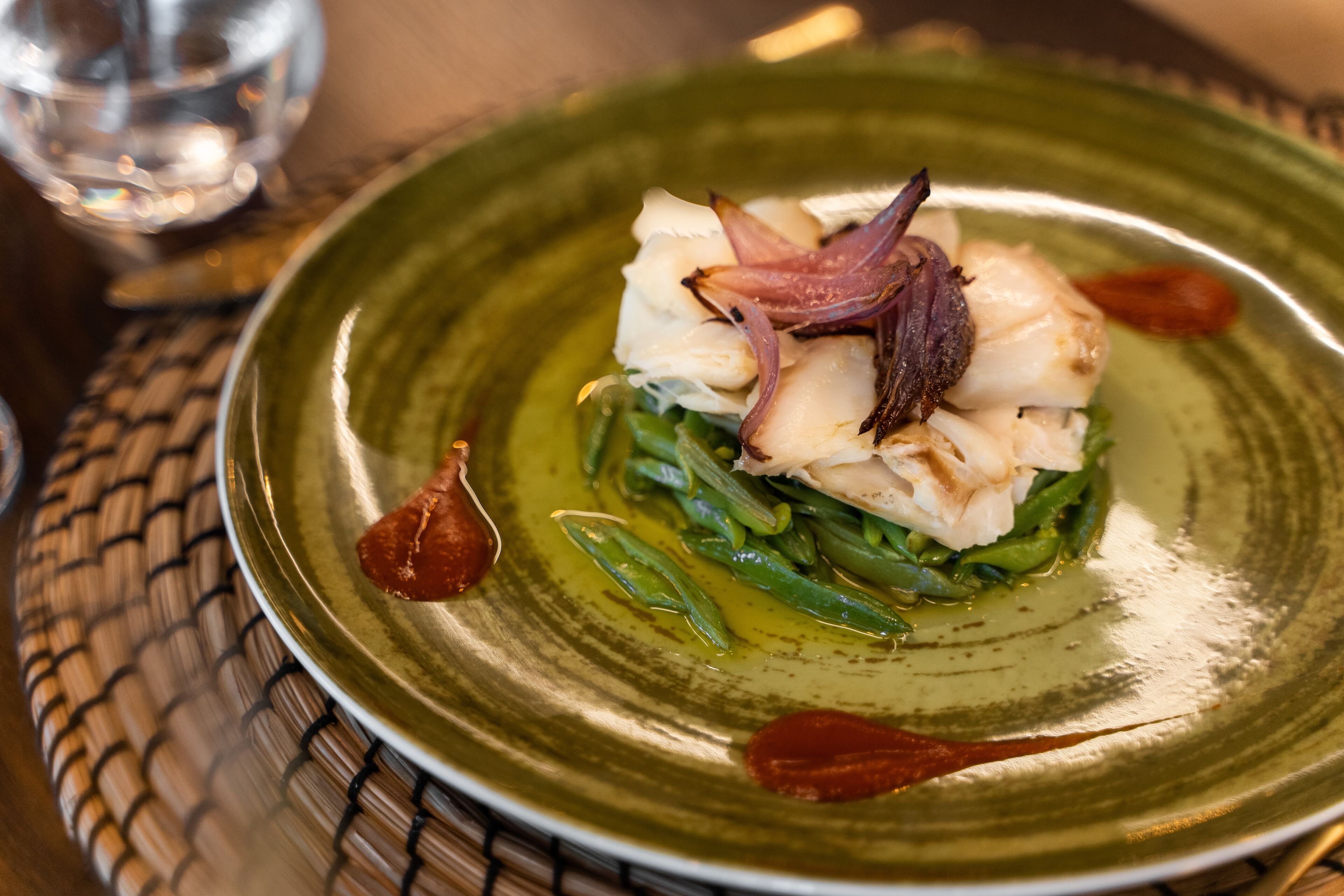 A plate of food with green beans, white fish, and red onions on a green plate.