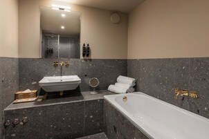 Un baño moderno con una bañera independiente, un lavamanos pedestal y un espejo grande.