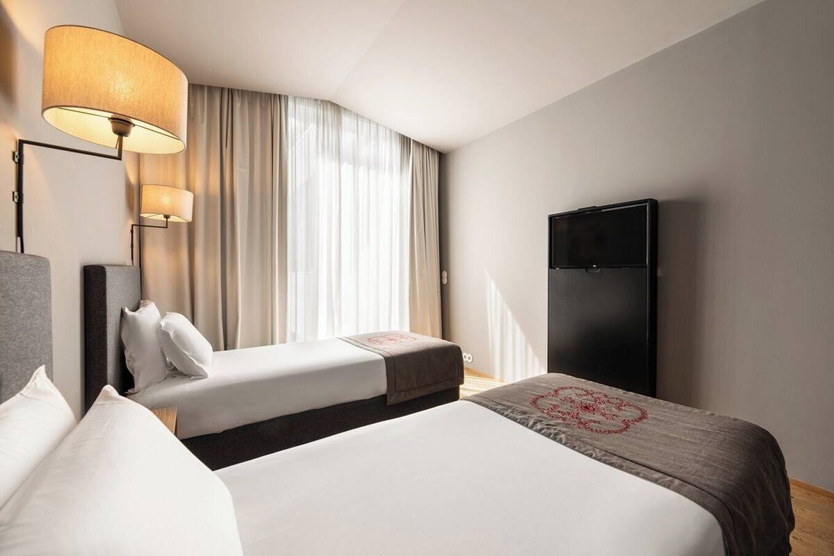 Een hotelkamer met twee bedden, een televisie, een lamp en een groot raam met gordijnen.