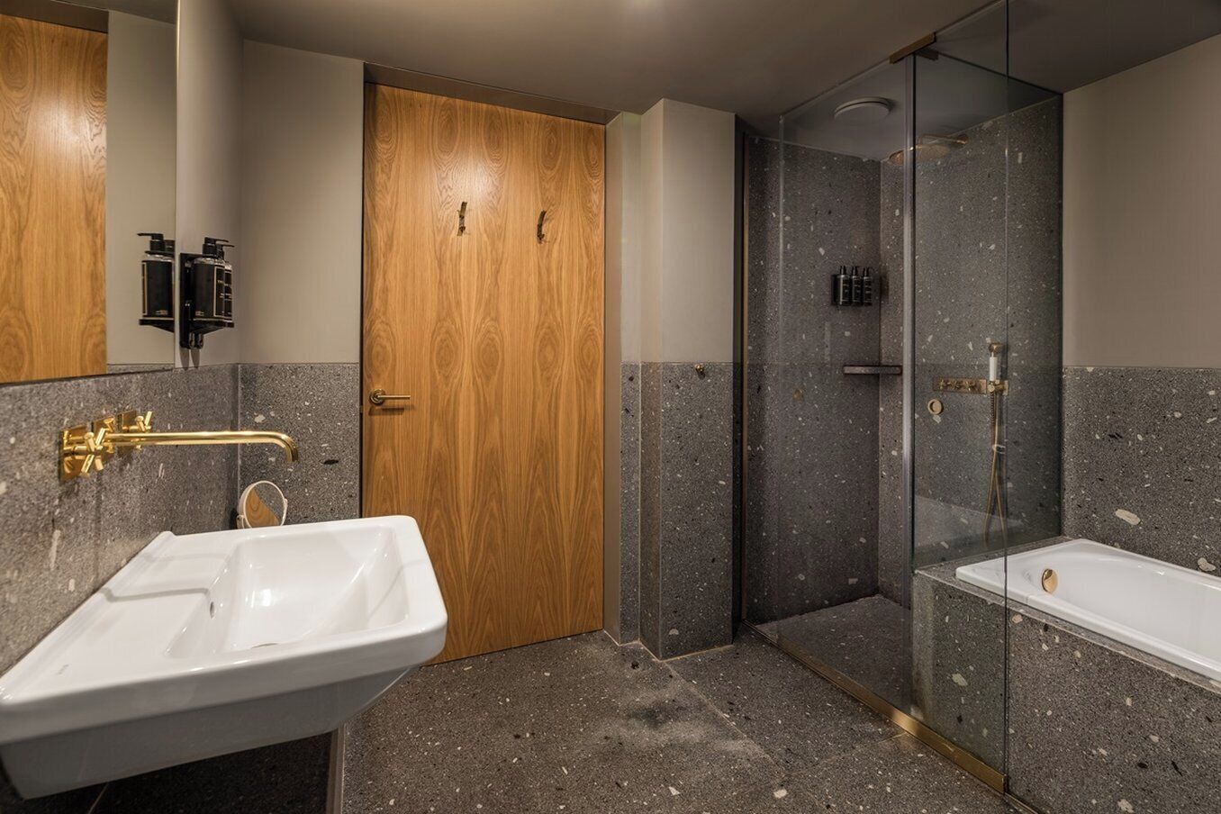Un baño con puerta de madera, lavamanos blanco, cabina de ducha con mampara de vidrio y bañera.