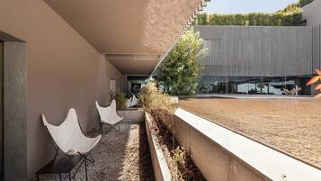 Un área de estar moderna al aire libre con sillas blancas y un camino de grava, que conduce a un edificio con fachada de madera vertical.