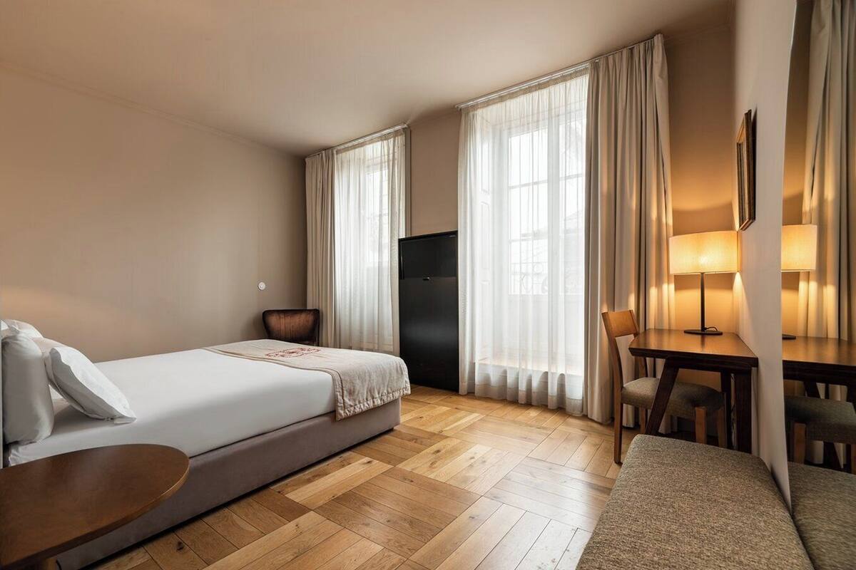Een hotelkamer met een bed, een bureau met stoel, een televisie en een lamp.