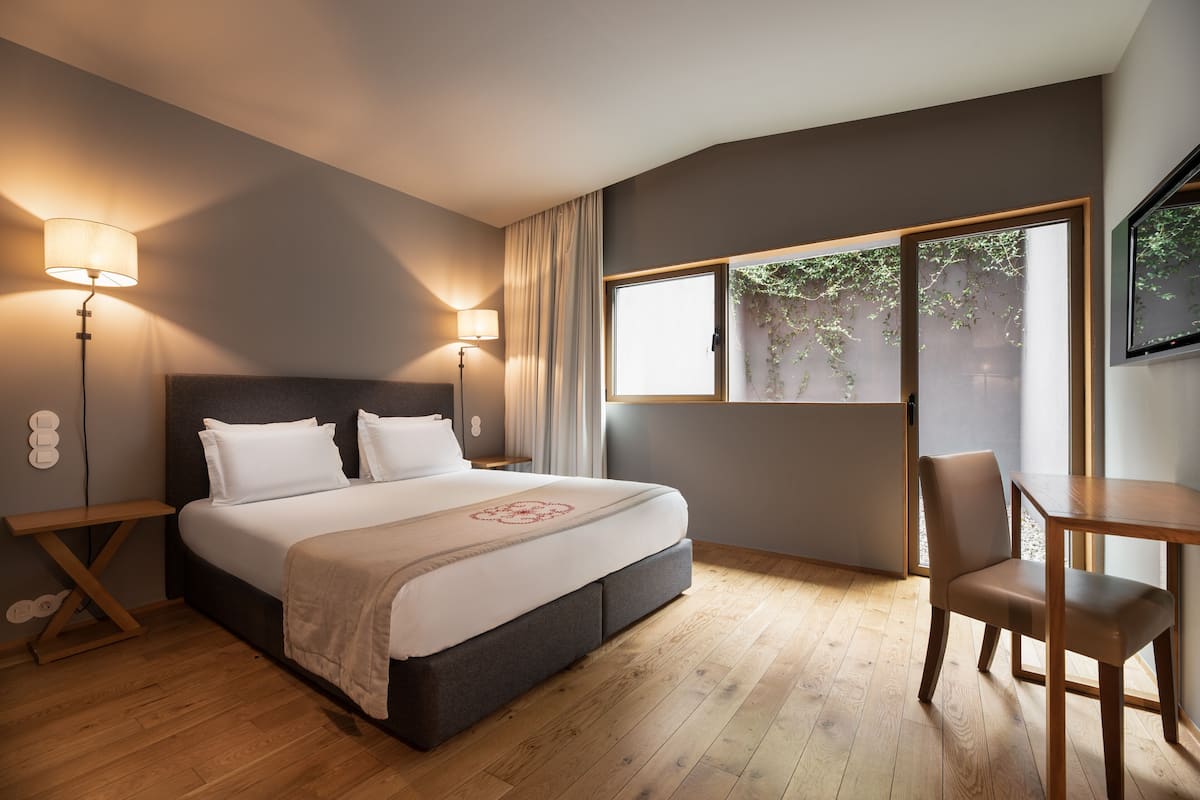Een slaapkamer met een bed, nachtlampjes, een stoel, een tafel en een raam met gordijnen.