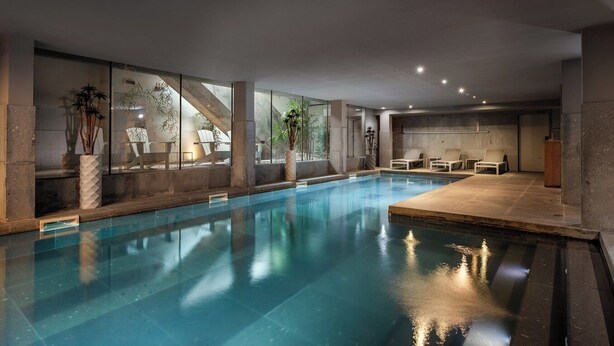Une piscine intérieure avec des parois en verre transparent, des chaises longues et des plantes en pot.