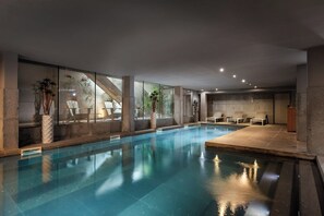 Une piscine intérieure avec des parois en verre transparent, des chaises longues et des plantes en pot.