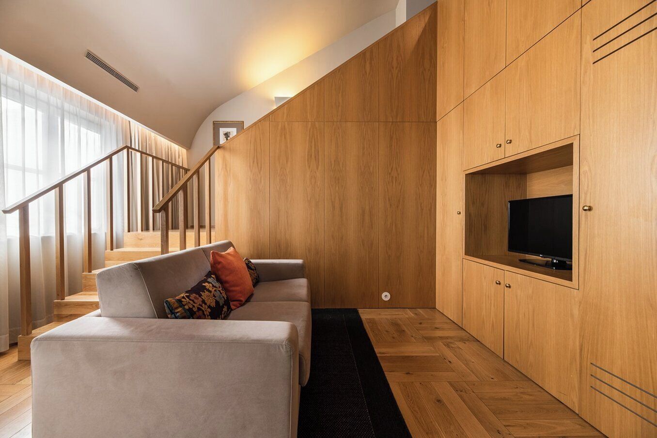 A modern living room with a grey sofa, wooden cabinets, and a TV on a wooden shelf.