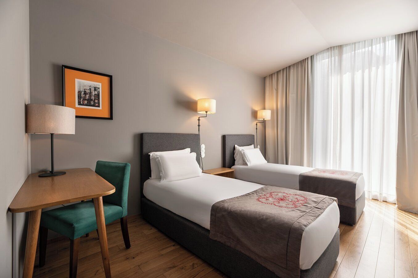 Une chambre d’hôtel avec deux lits, un bureau, une chaise et une grande fenêtre avec des rideaux.