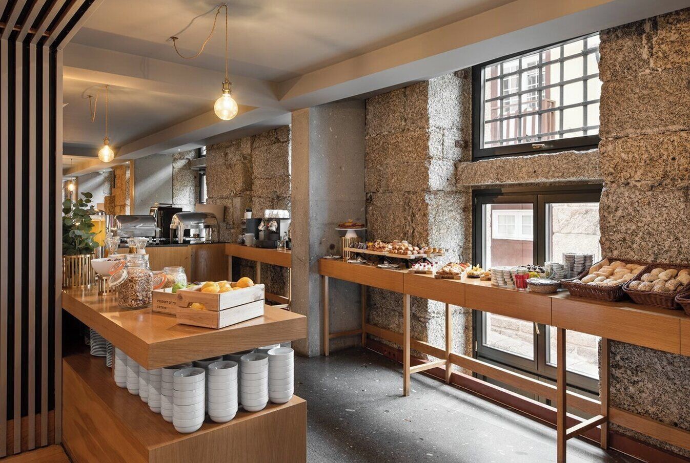 A cafe with a rustic stone wall, wooden counter, and various baked goods displayed.