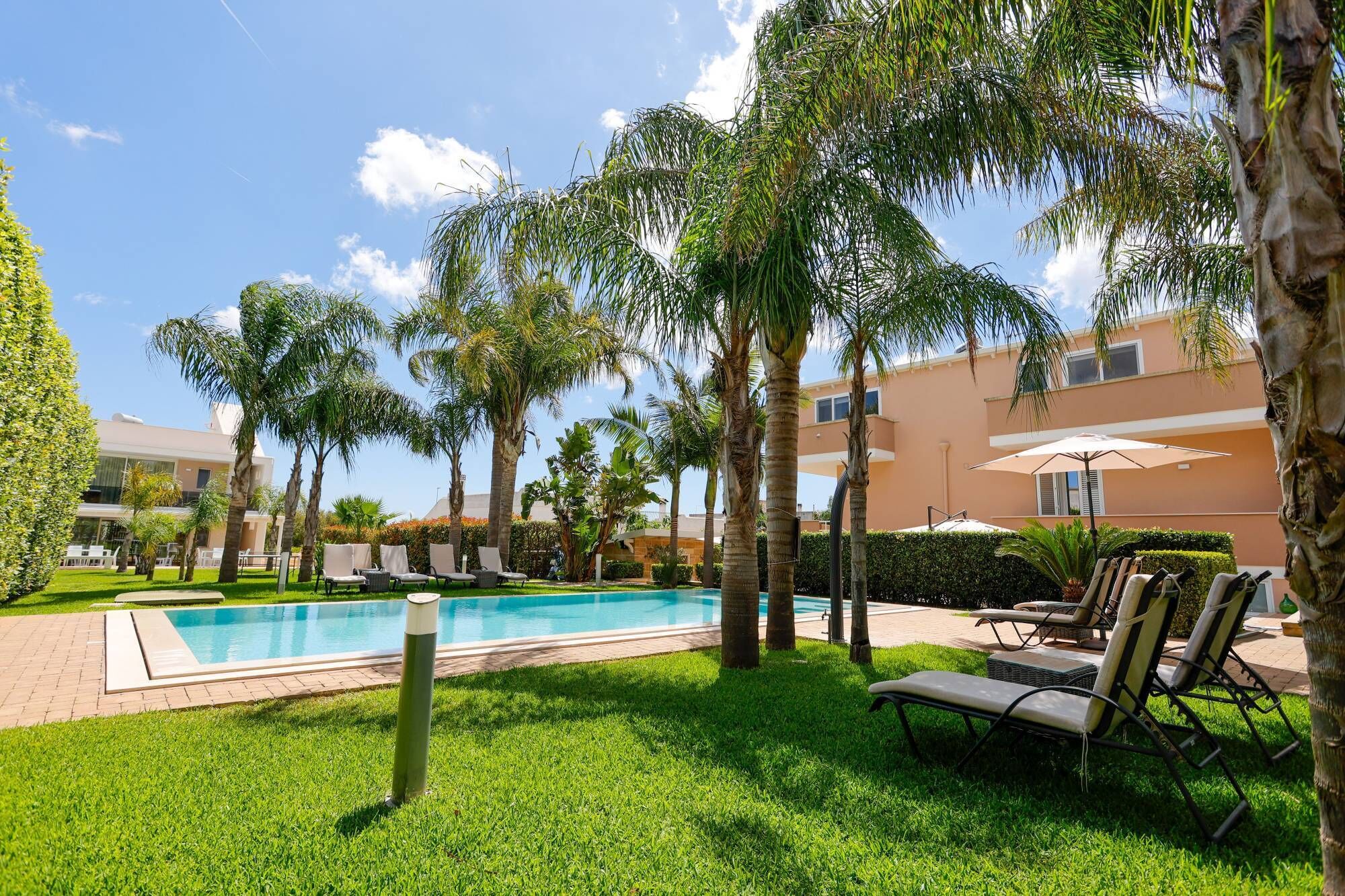 A pool area with lounge chairs, palm trees, and a building in the background.