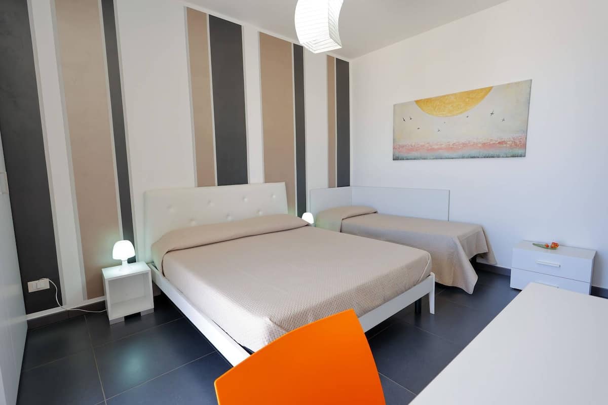 A hotel room with two beds, a desk, and a painting on the wall.