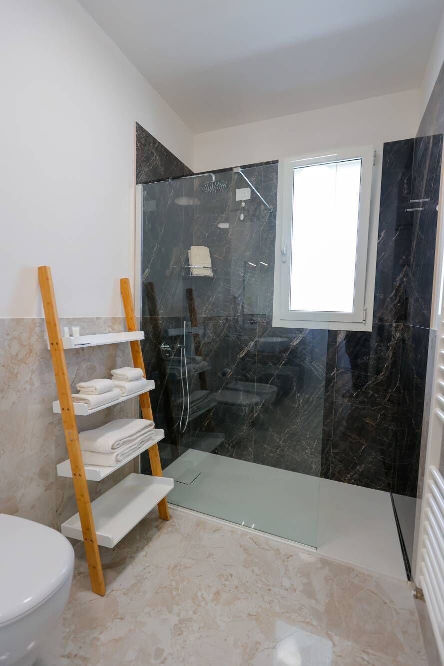 A bathroom with a glass shower enclosure, a wooden shelf with towels, and a white toilet.
