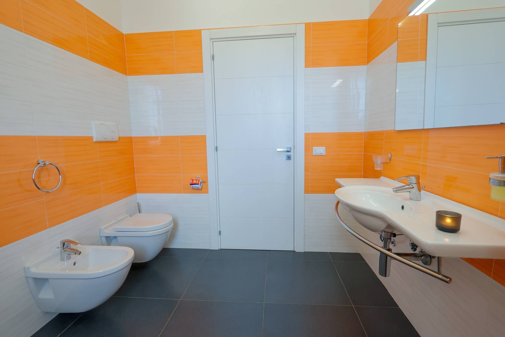 A bathroom with a toilet, bidet, and sink, featuring orange and white tiles.