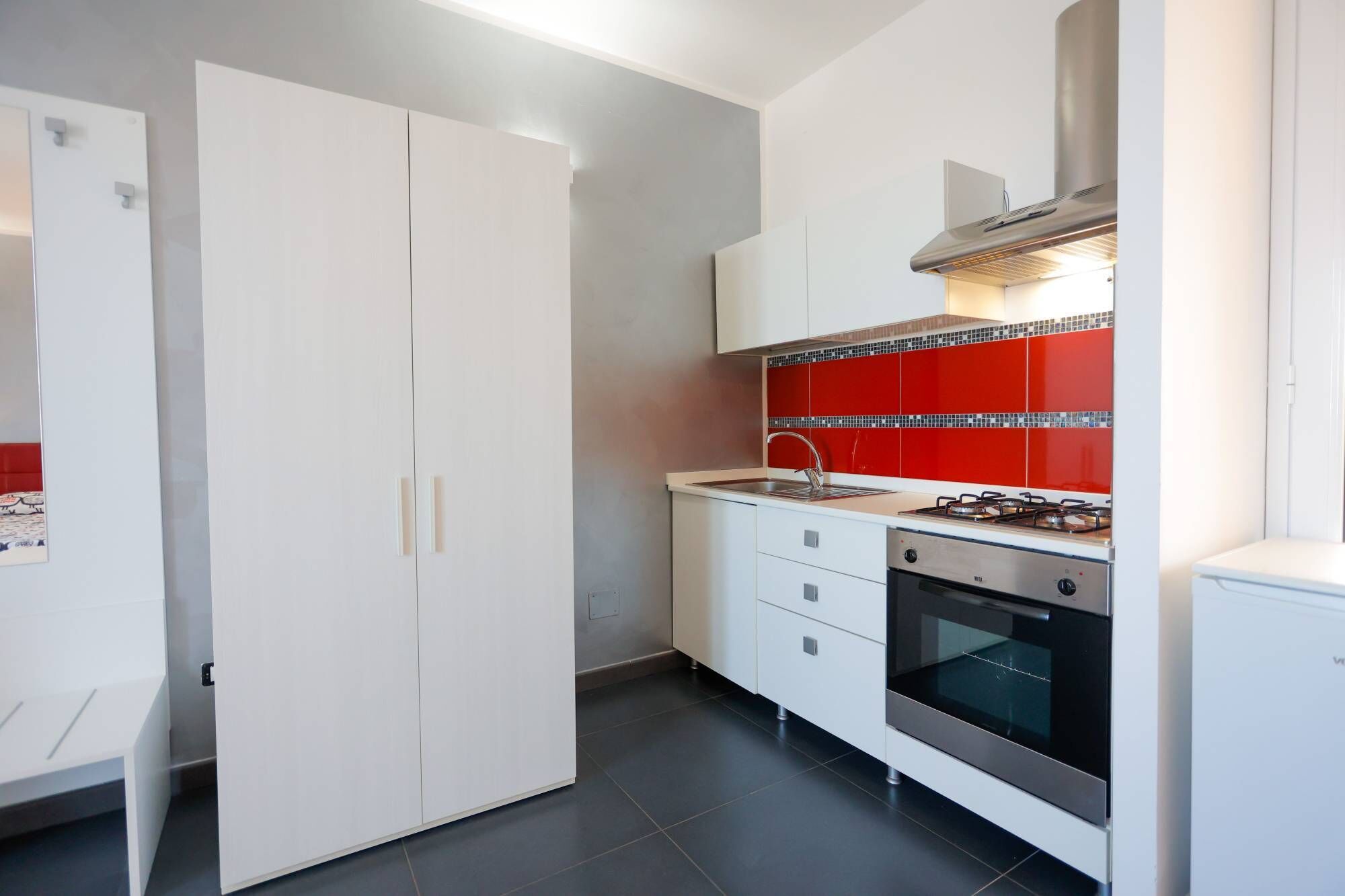 A kitchen with white cabinets, a red backsplash, a stove, and an oven.