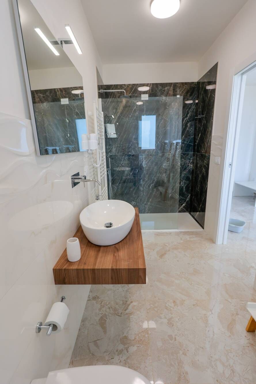 Un baño moderno con un lavabo grande de color blanco, un mueble de tocador de madera, una cabina de ducha de vidrio y un suelo de mármol.