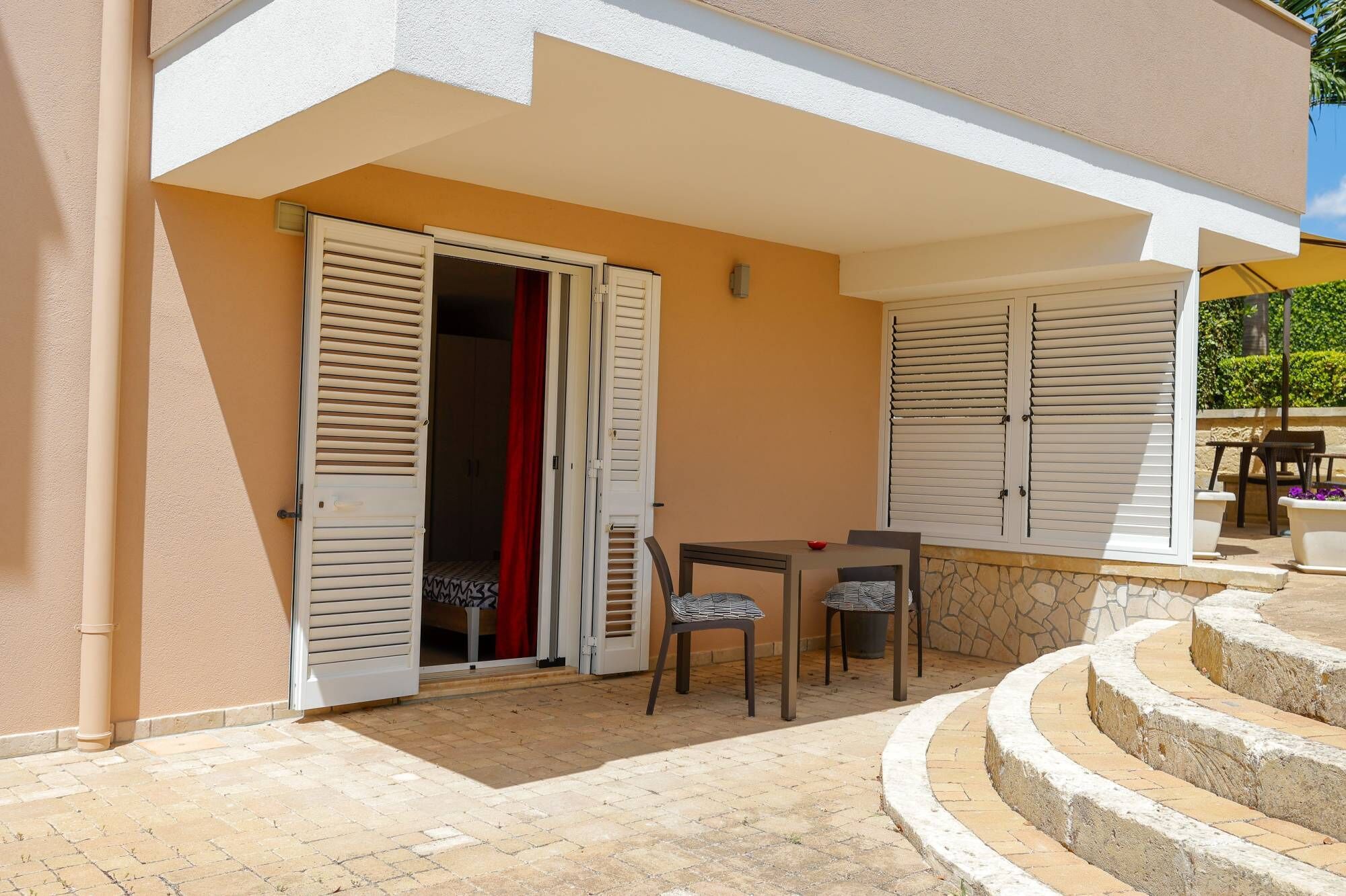 Un patio con mesa y sillas, una cortina roja y una escalera que lleva a un espacio exterior con asientos.