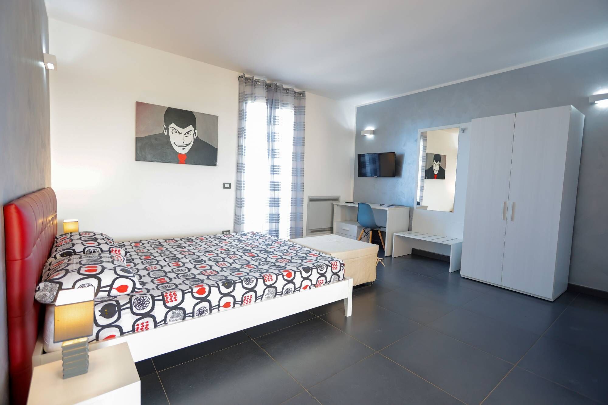A bedroom with a bed, a desk, a chair, a wardrobe, and a TV.