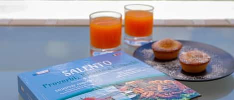 A book titled 'Salento' and two glasses of orange juice on a table with a view of a garden.