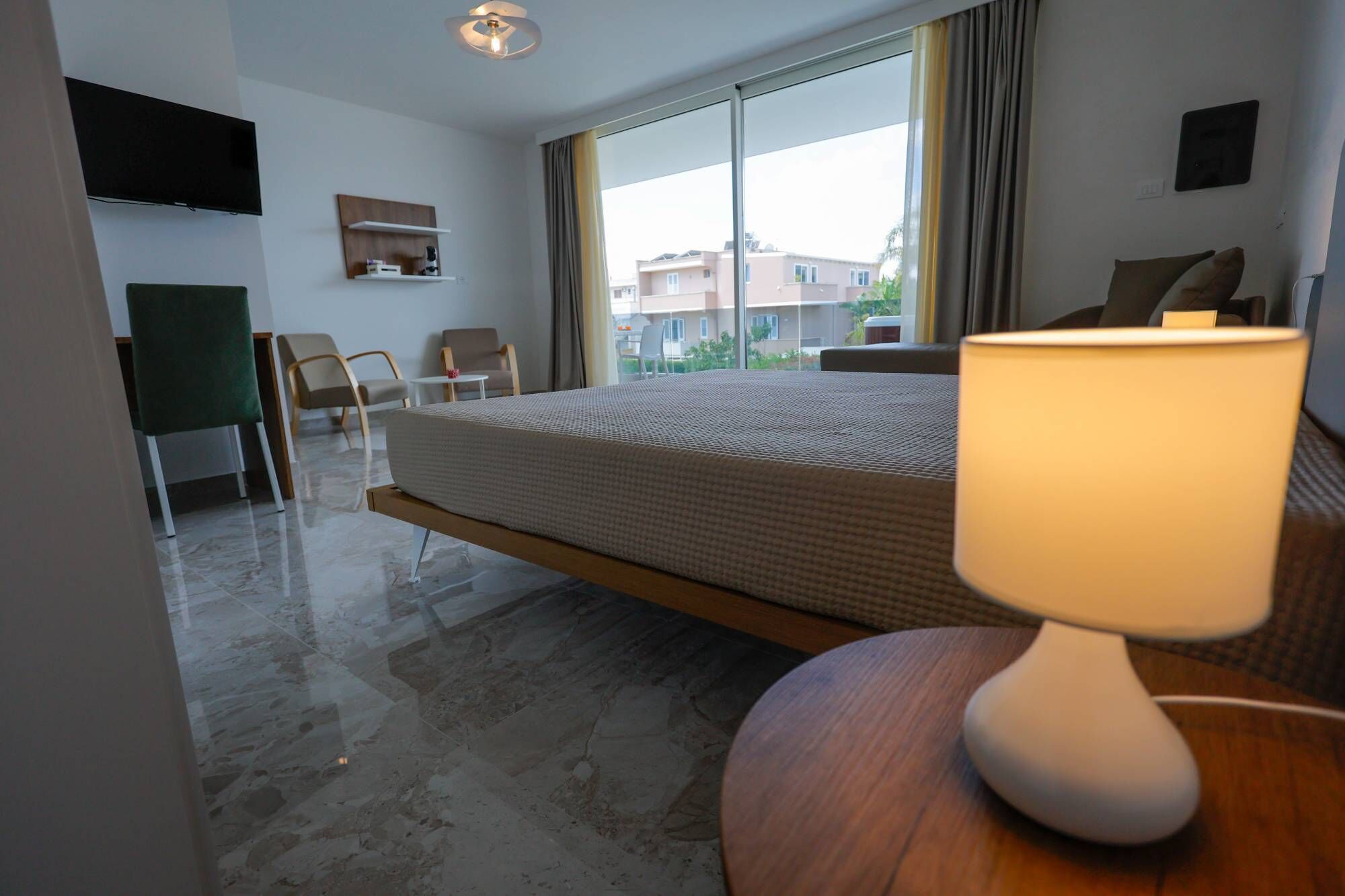 Ein Hotelzimmer mit einem Bett, einem Schreibtisch, einem Sessel, einem Fernseher und einem Fenster mit Blick auf Gebäude.