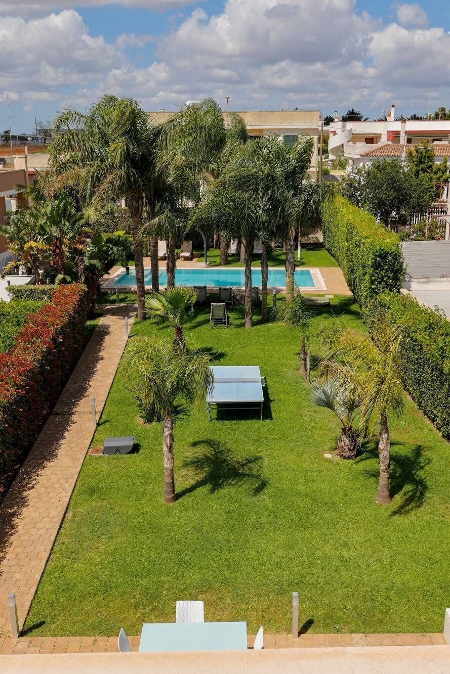 Un jardín bien cuidado con piscina, palmeras y sillones de descanso.