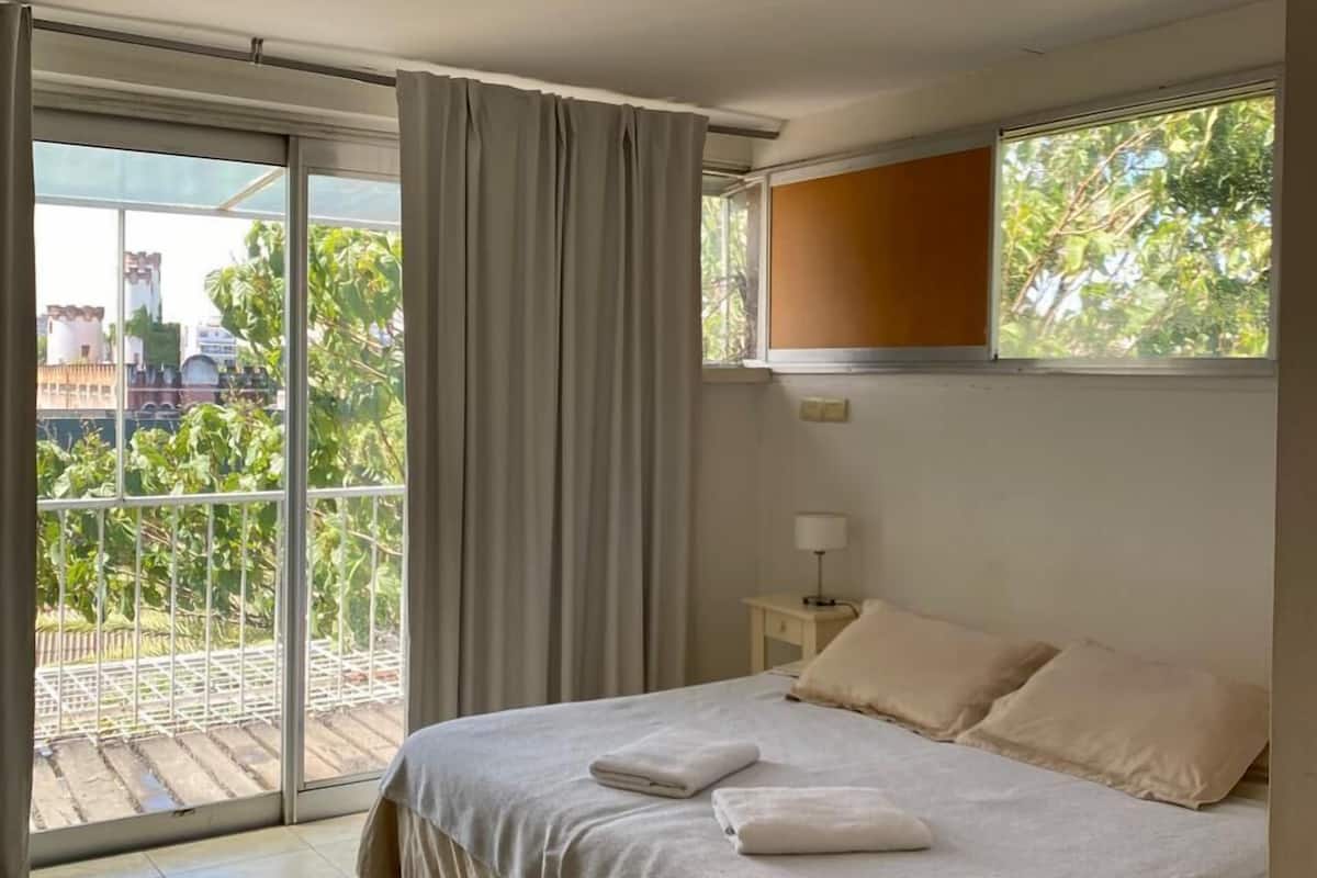 A bedroom with a bed, a window, a nightstand, and a view of greenery outside.