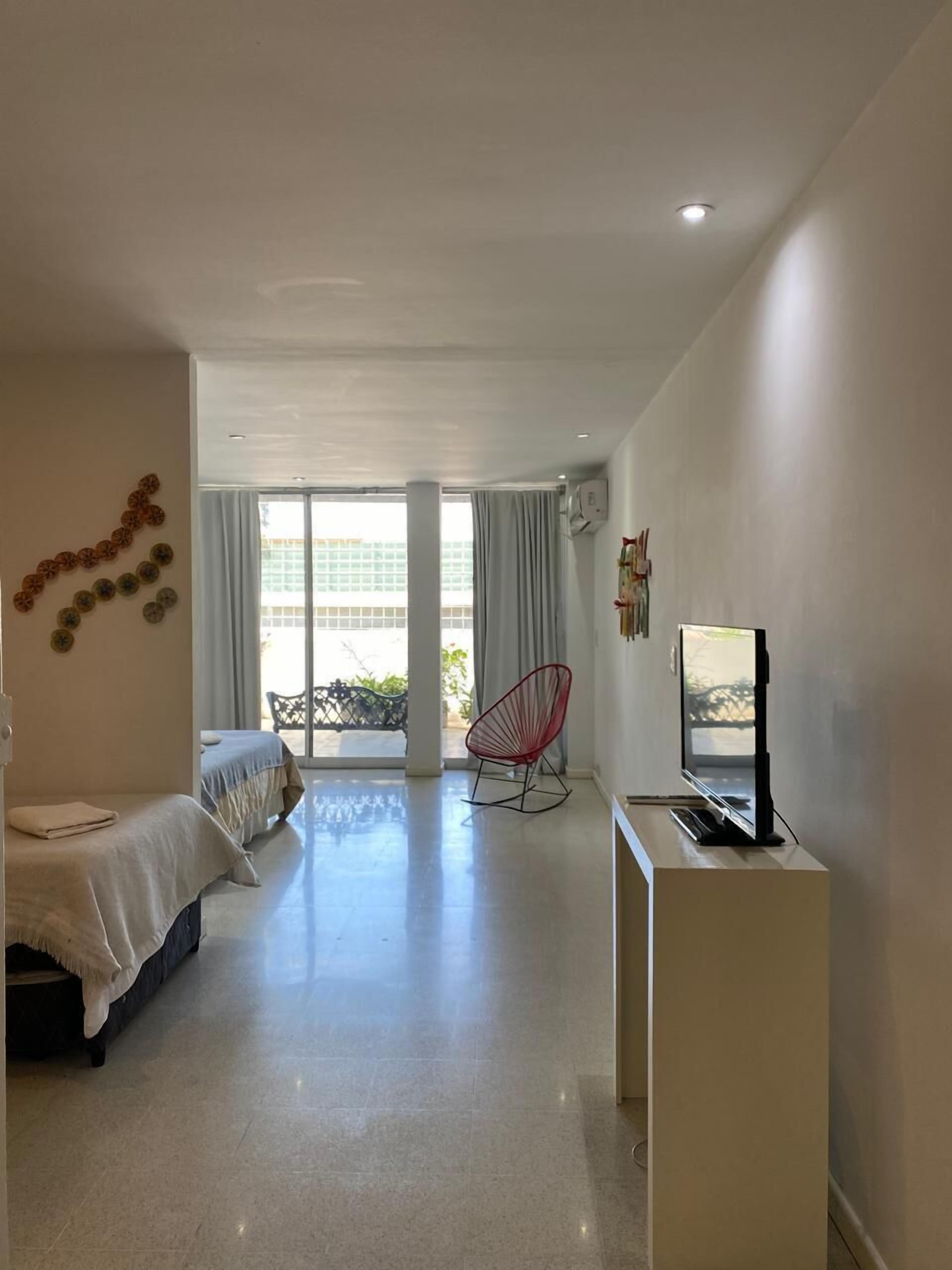 A modern hotel room with a bed, a TV, a red chair, and a balcony with a view.