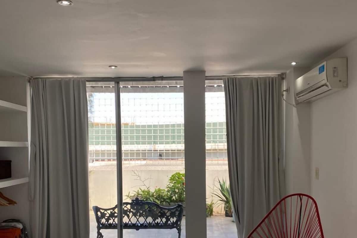 A hotel room with a bed, a red chair, a balcony with a view, and a ceiling light.