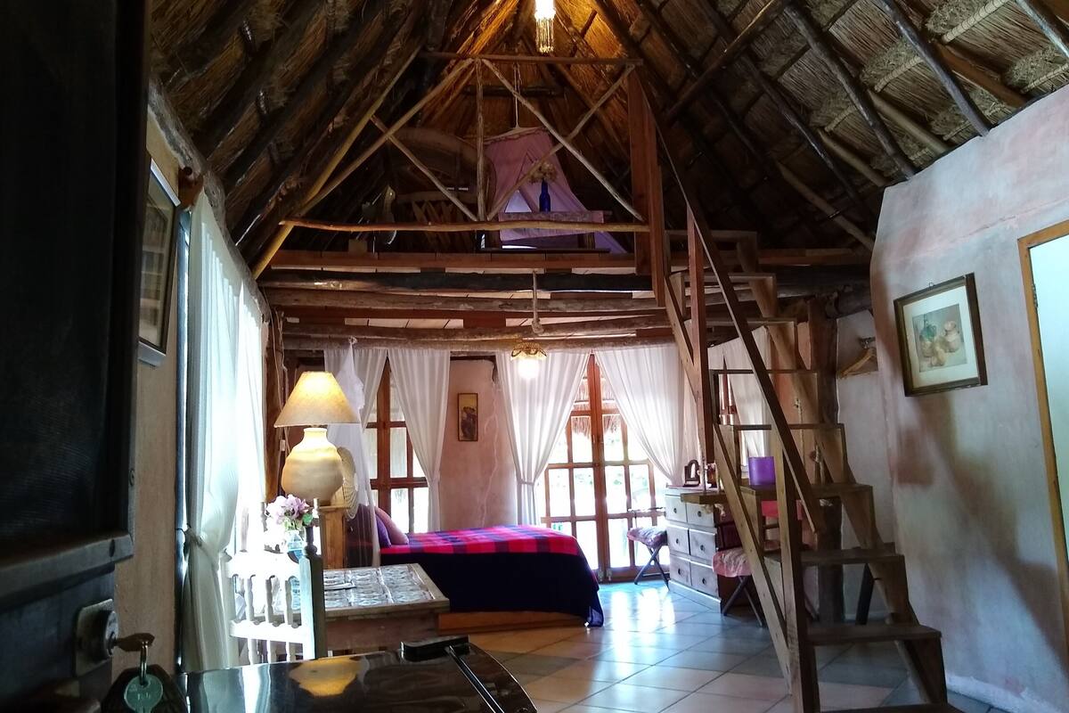 Una habitación rústica con techo inclinado, una cama con una colcha roja, una escalera de madera y una escalera.
