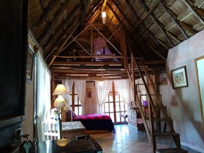 A rustic room with a sloped ceiling, a bed with a red blanket, a wooden ladder, and a staircase.