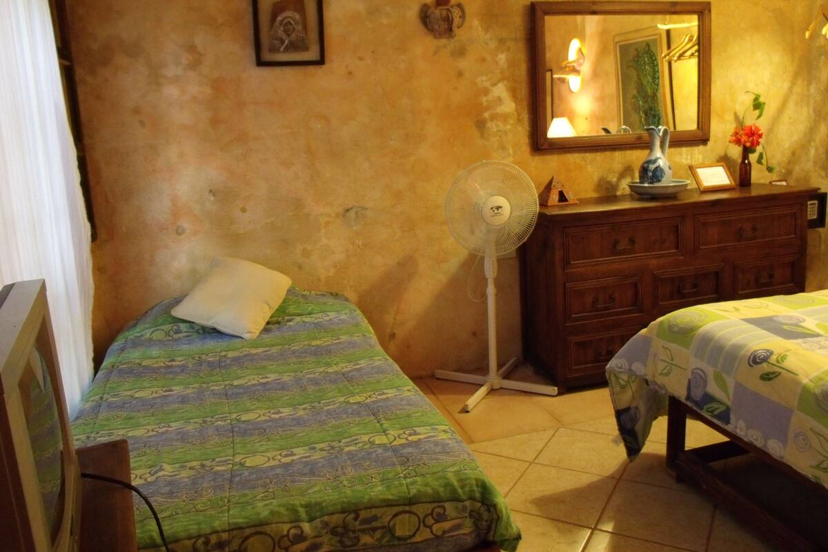 Una habitación con dos camas, un aparador, un ventilador y un espejo en la pared.