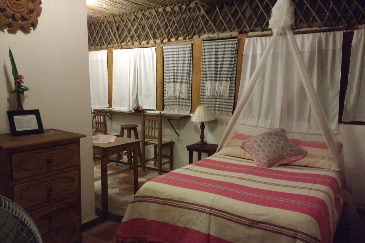 Una habitación con cama, escritorio, silla, mesita de noche y cómoda.