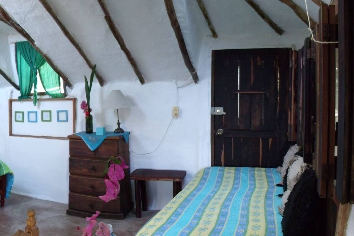 Una habitación rústica con techo de madera, una cama con colcha a rayas, un tocador y un espejo.