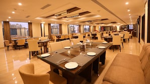 A spacious dining area with multiple tables and chairs, large windows, and a modern ceiling design.