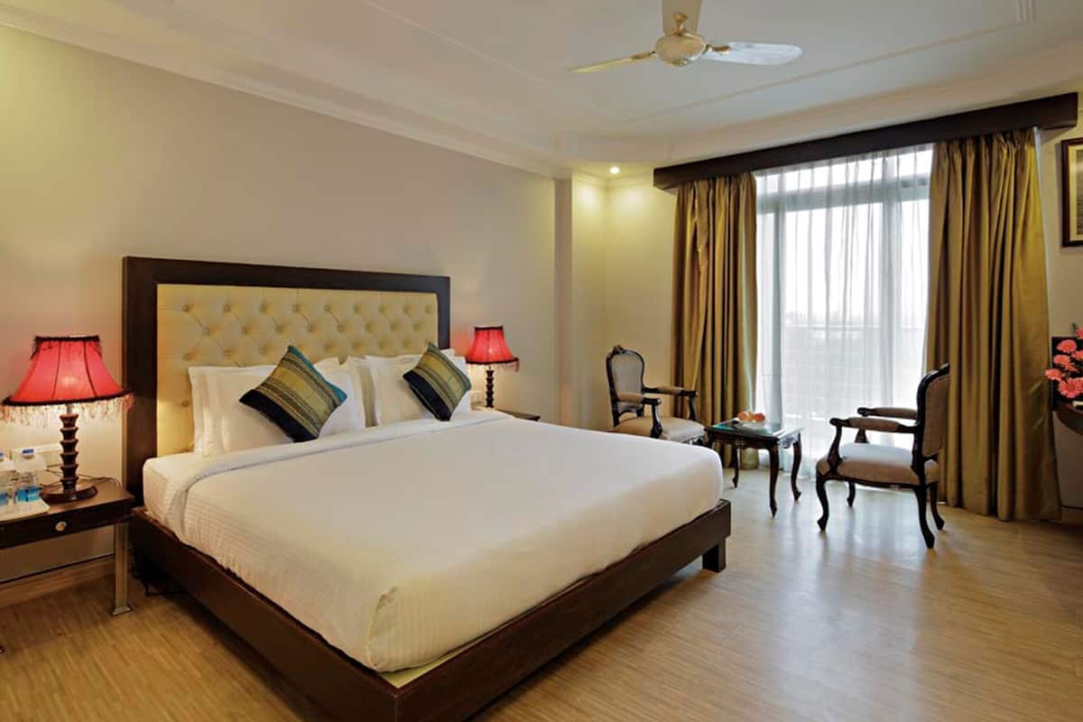 A hotel room with a large bed, two bedside lamps, a ceiling fan, a desk with a chair, and a window with curtains.
