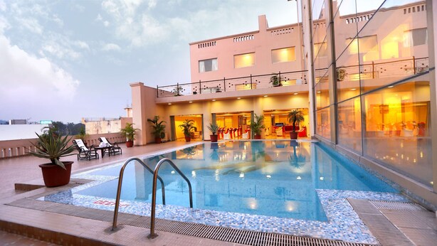 A rooftop swimming pool with lounge chairs and potted plants, surrounded by a building with multiple balconies and large windows.