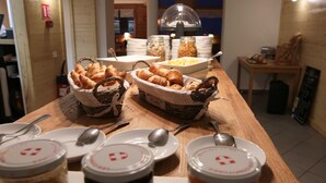 Un buffet de petit-déjeuner comprenant des croissants, des pâtisseries et des fruits présentés dans des paniers, ainsi que des assiettes et des condiments.