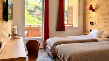 A hotel room with two beds, a desk, a chair, and a window with curtains.