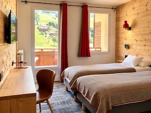 Een hotelkamer met twee bedden, een bureau, een stoel en een raam met gordijnen.