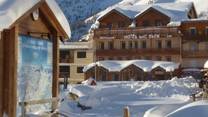 Une station de montagne enneigée, avec des bâtiments en bois, notamment un restaurant, un hôtel et un bar.