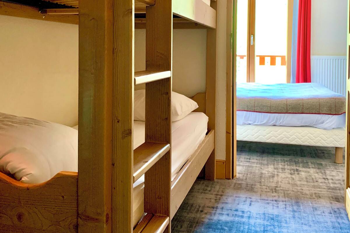 Een kamer met stapelbedden, een blauw tapijt en uitzicht op een balkon met rode gordijnen.