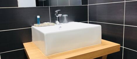 Een badkamer met een wit wastafel, houten opbergmeubel en zwart betegelde wanden.