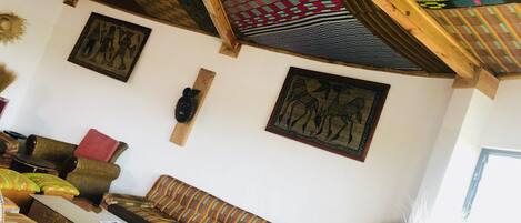 Una habitación con techo alto, vigas de madera, techo con diseño, un sofá, una pequeña mesa y obras de arte colgadas en la pared.