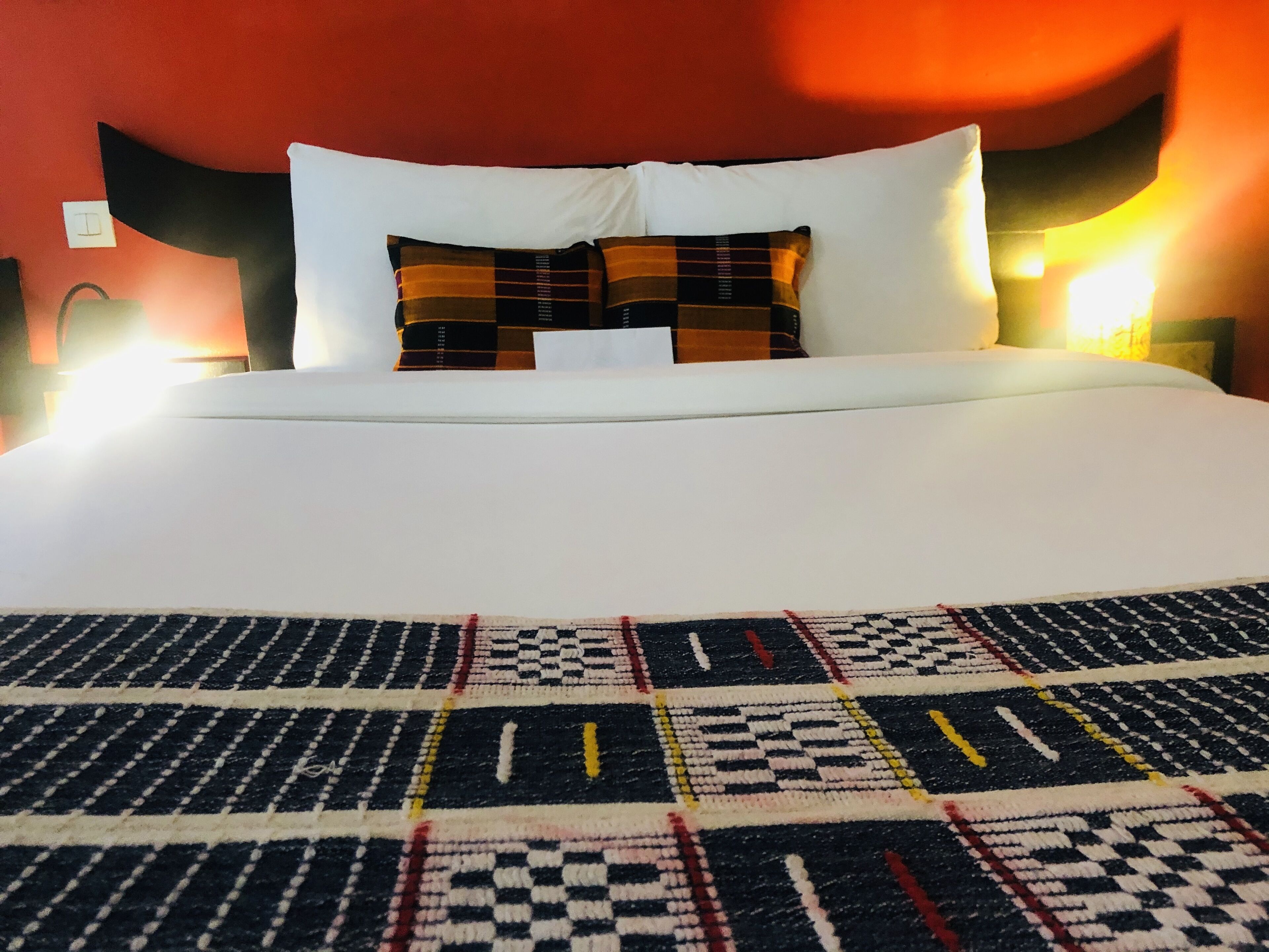 A bed with a patterned blanket, white pillows, and a red wall.