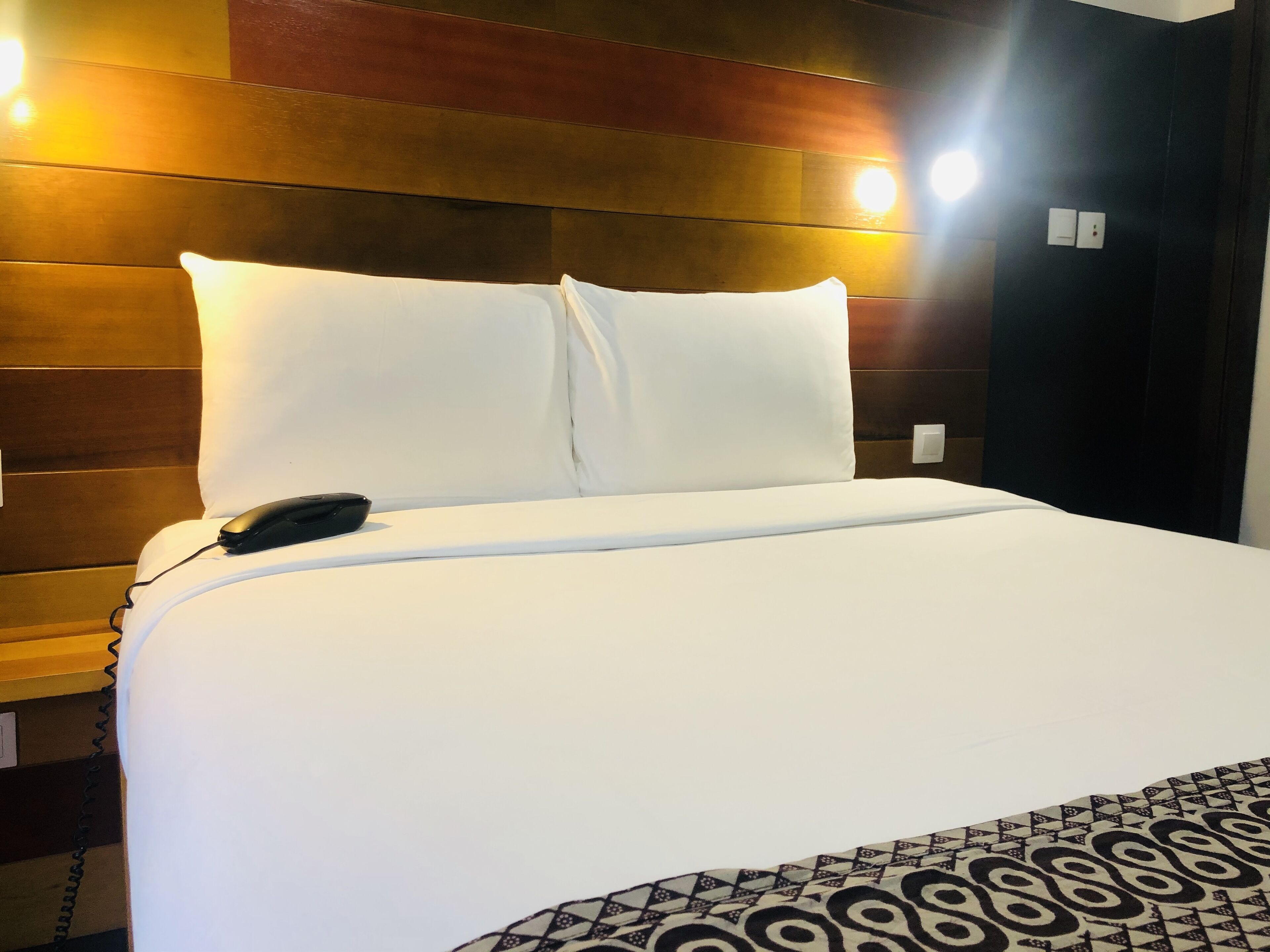 A neatly made bed with white linens and a patterned throw blanket.
