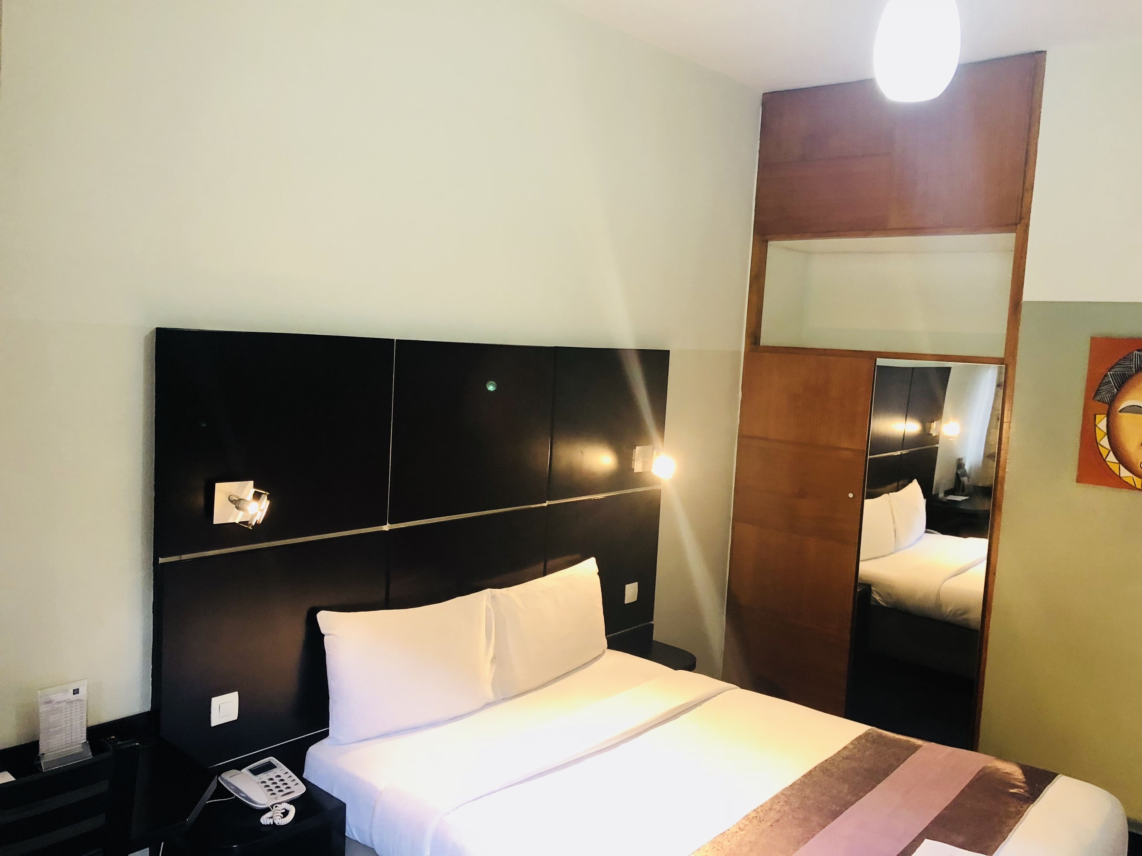 Een hotelkamer met een groot bed, een nachtkastje met een telefoon en een spiegel aan de muur.