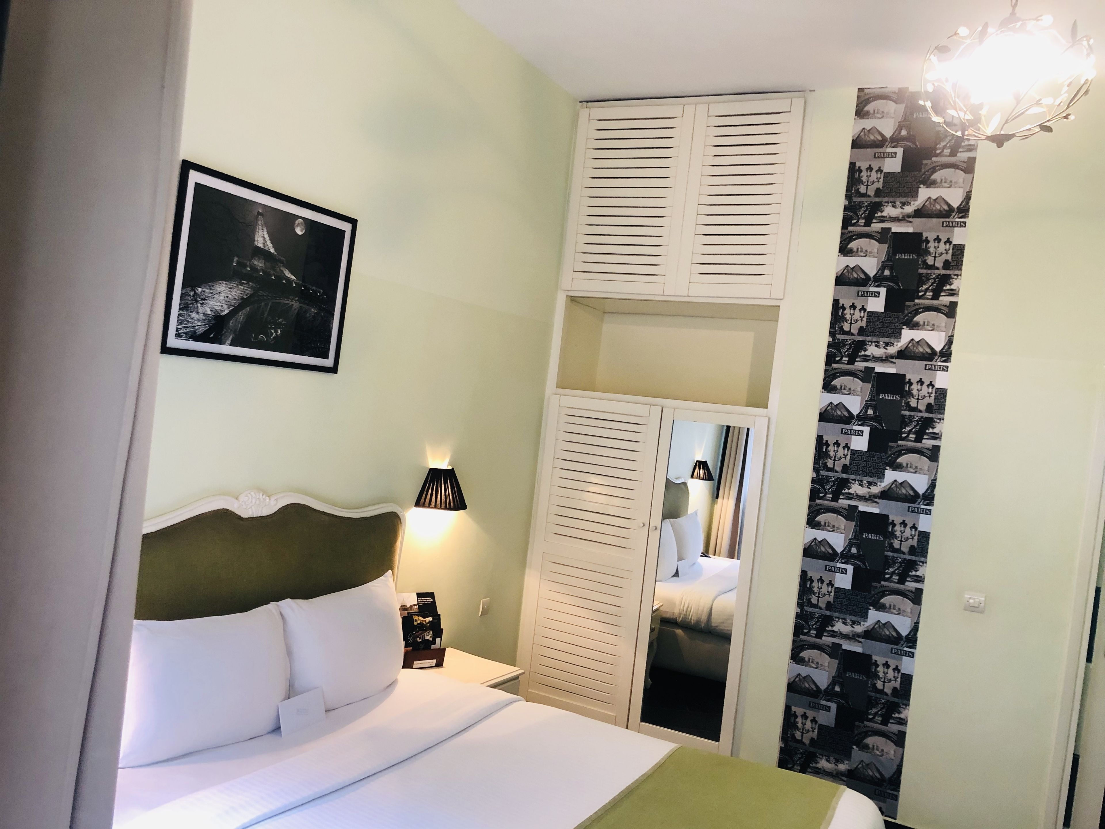 Een hotelkamer met een bed, nachtkastje, lamp, kast en gordijnen met Parijse motieven.
