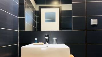 A bathroom with a white sink, dark tiled walls, and a mirror reflecting a door and a view.