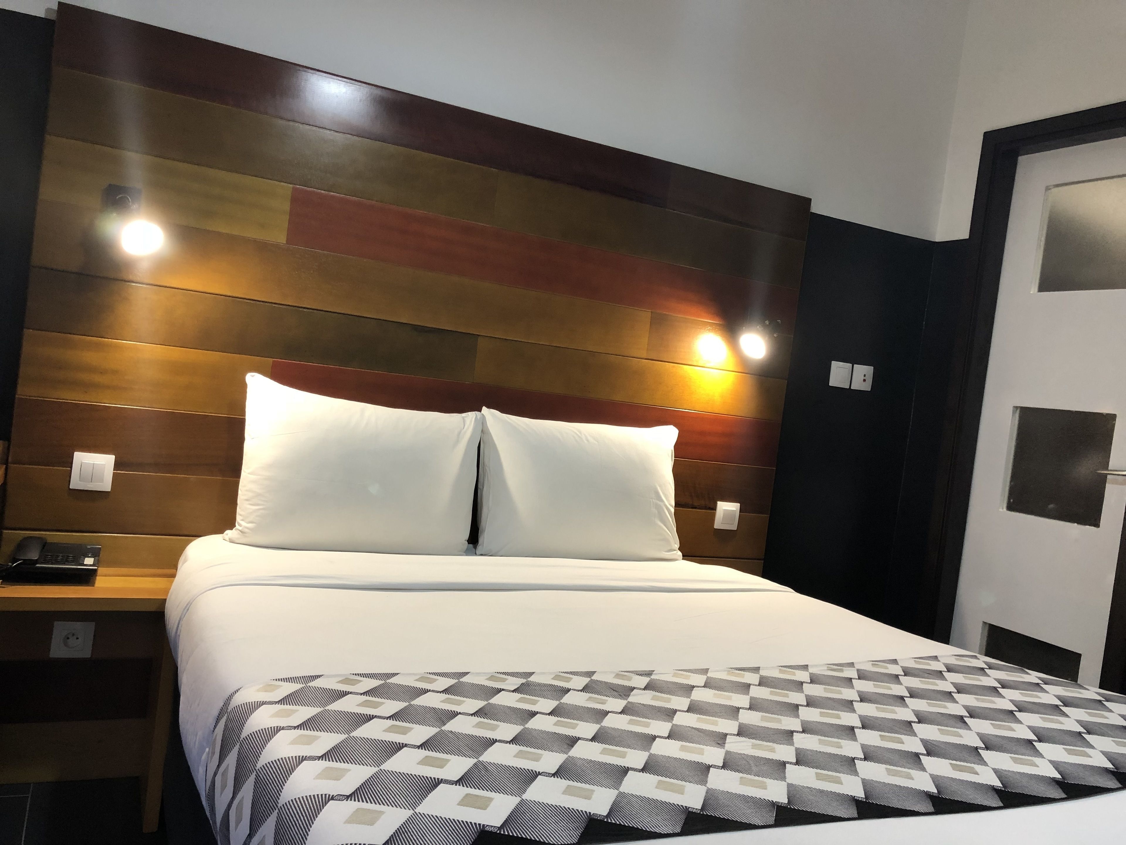 A hotel room with a bed, a nightstand, and a wall-mounted light fixture.