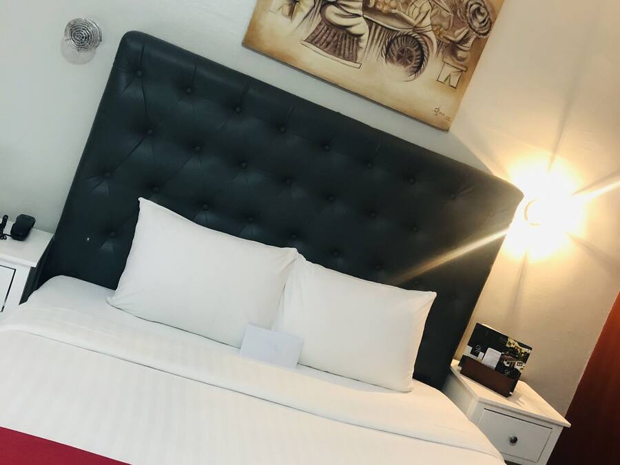 A hotel room with a large bed, a dark headboard, a bedside table with a lamp, and a wall-mounted artwork.