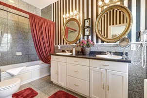 A bathroom with a white vanity, two large mirrors, a sink, and a bathtub.