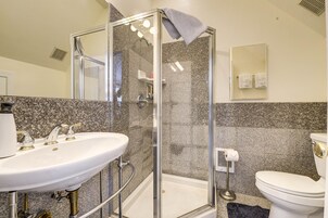 Un baño con ducha compartimentada con vidrio, un lavamanos blanco y un inodoro.